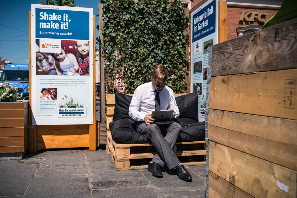 Mann sitzt mit Tablet am Bahnhof Pasing